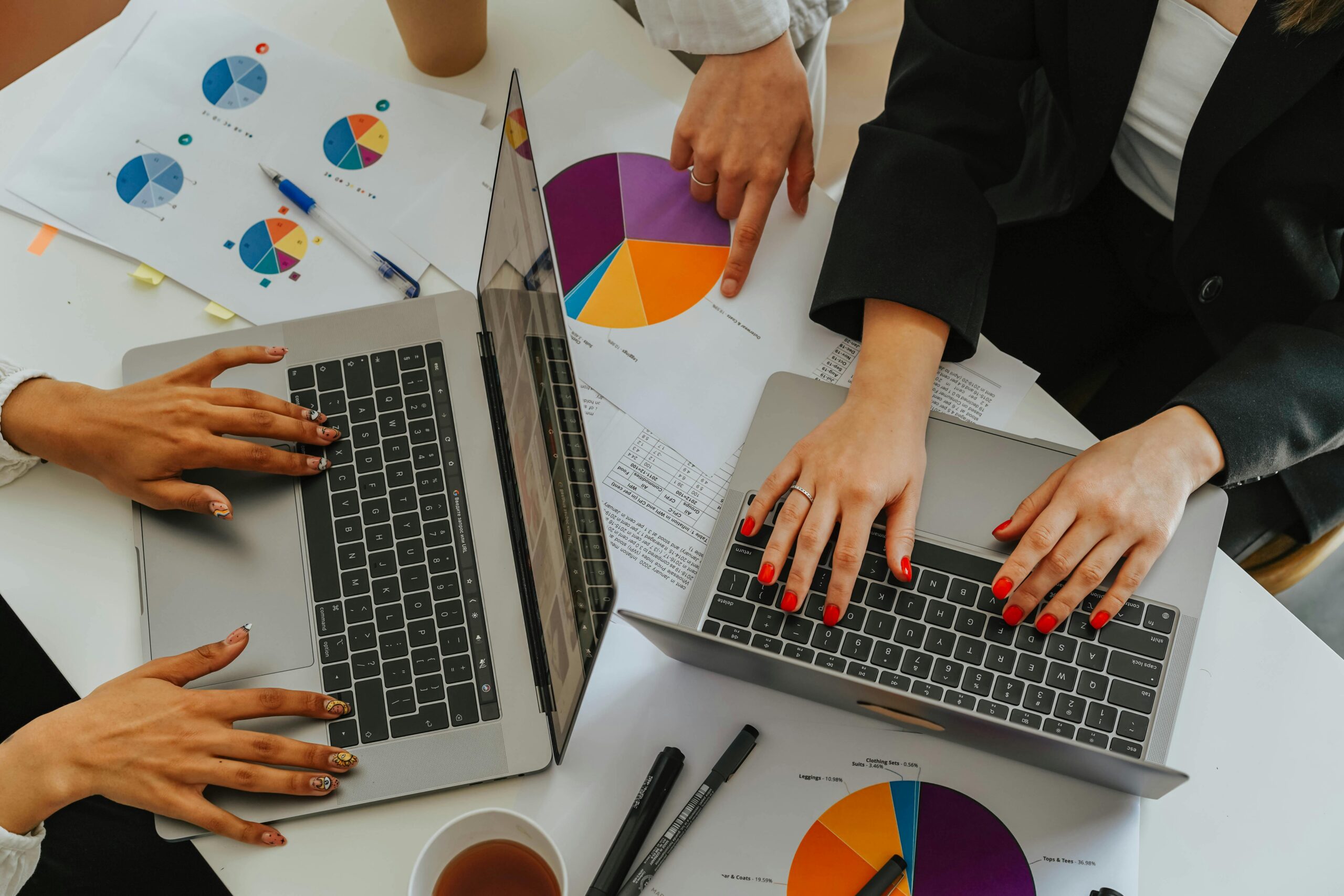 Top view of women working together on laptops with business charts at a white office table.